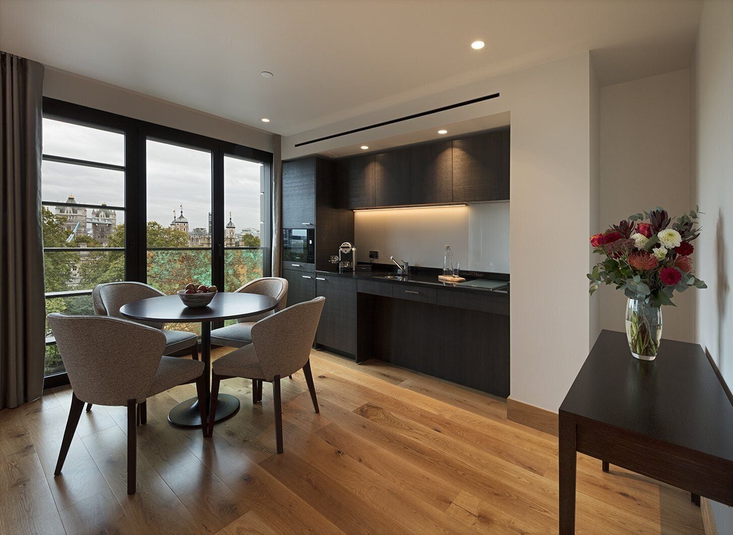 A modern kitchen with dark cabinetry, a central island, and a dining area with chairs.
