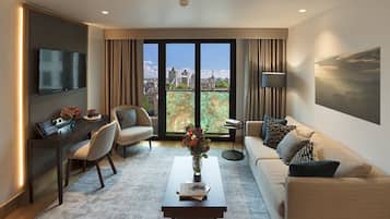 Una sala de estar moderna con sofá, sillón, mesa de centro y escritorio con ordenador. Un amplio ventanal ofrece vista a la ciudad.