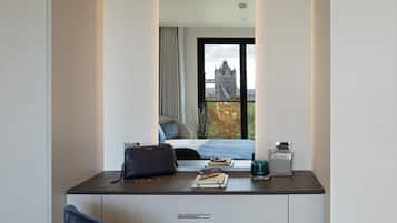 Une chambre moderne avec un grand miroir, un bureau avec un ordinateur portable, une chaise et une vue sur un pont et un immeuble.