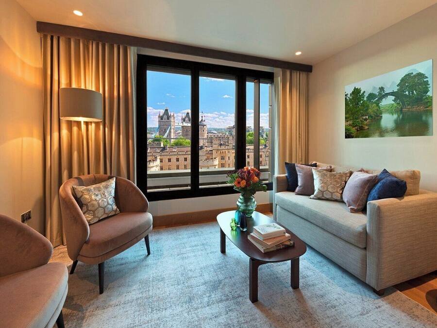 A modern living room with a sofa, armchair, and coffee table, a large window with a city view, and a painting on the wall.