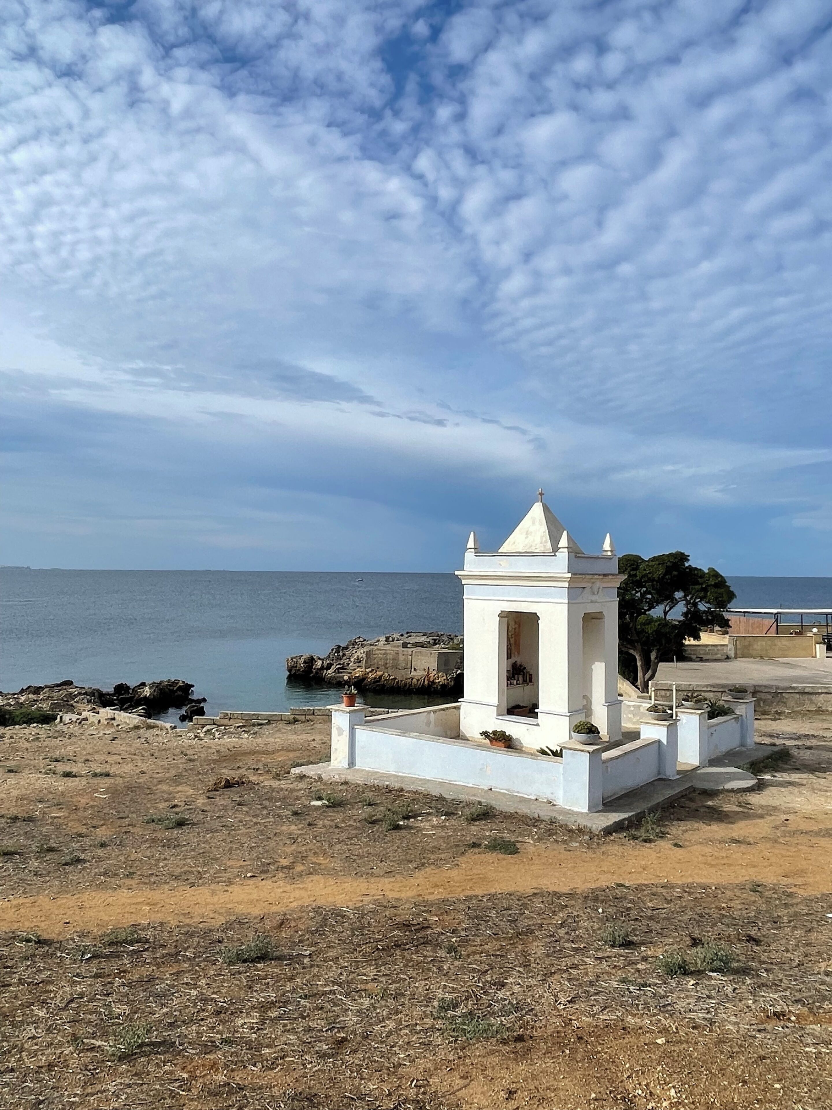 A small white structure with a pointed roof, situated on a rocky terrain near a body of water.