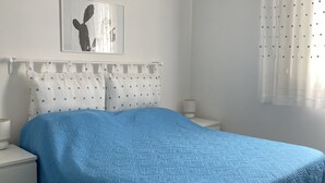 Ett sovrum med en säng, en takfläkt, ett nattduksbord, en lampa, en inramad tavla på väggen och ett fönster med gardiner.