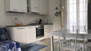 Ett modernt kök med vita skåp, en inbyggd ugn och en matplats med ett glasbord och vita stolar.