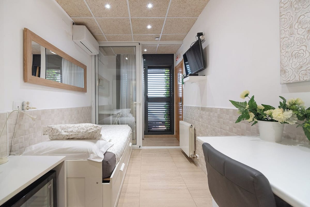 Quarto de hotel pequeno com uma cama, uma mesa, uma cadeira, uma TV e uma planta em vaso.