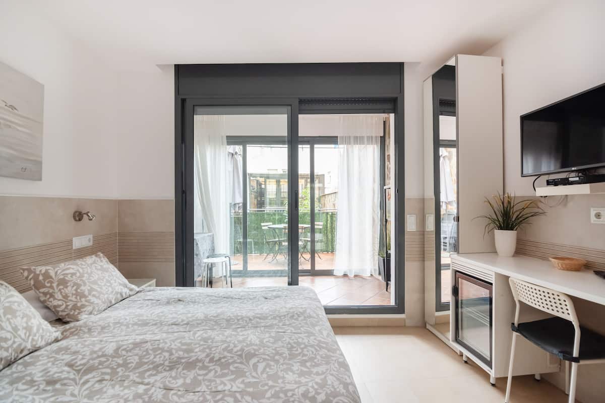 Quarto com cama, escrivaninha, televisão e porta de vidro deslizante que dá para área externa.
