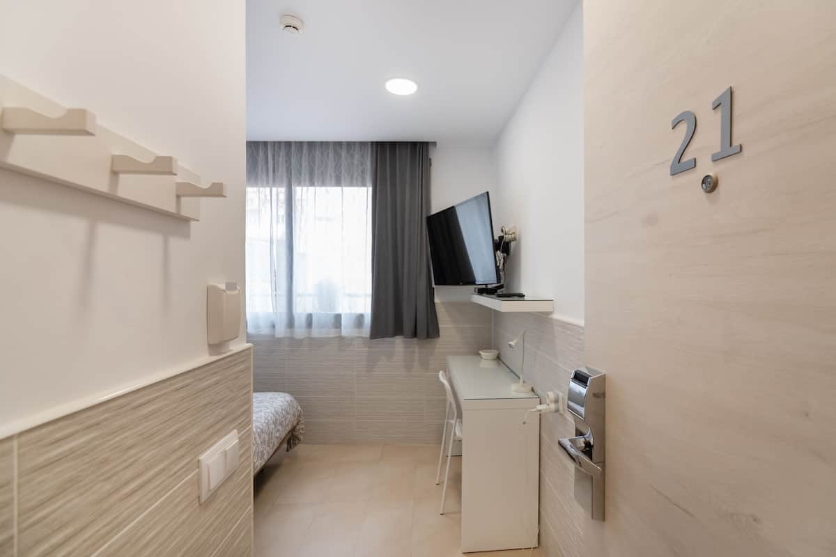 Quarto de hotel moderno com cama, escrivaninha, televisão e área de chuveiro.