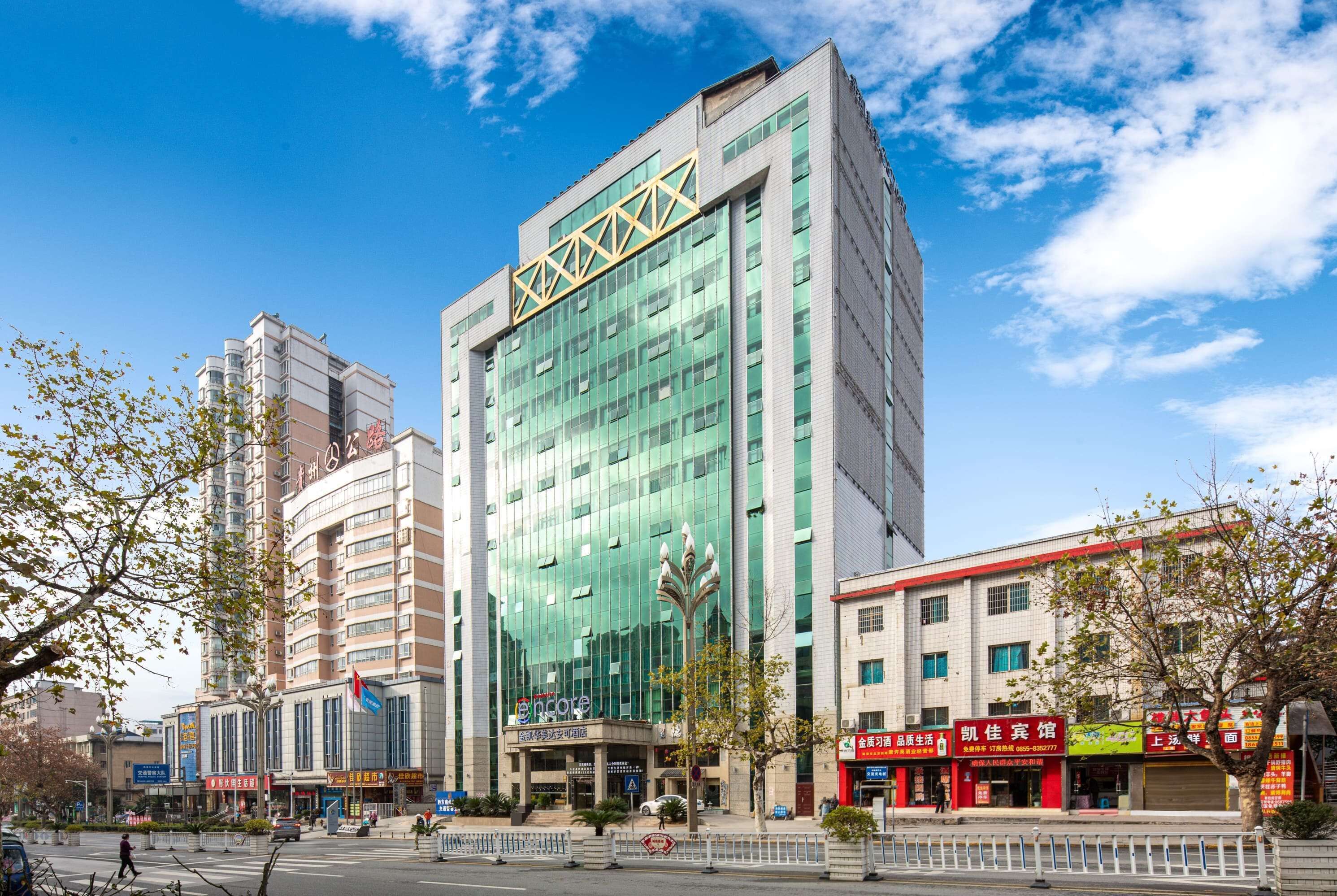 Et moderne hotel med en glasfacade, et tydeligt logo og et traditionelt kinesisk arkitektonisk element på taget.