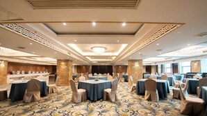 Un amplio salón de banquetes con mesas redondas, sillas color beige y una alfombra estampada.