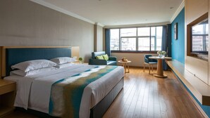 Habitación de hotel con una cama grande, un escritorio, una silla y vistas a la ciudad a través de las ventanas.