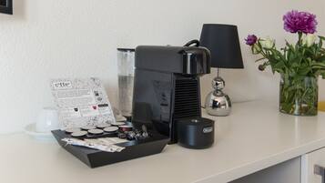 Una cafetera, una lámpara y un jarrón con flores sobre una mesa.