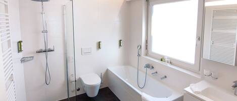 A modern bathroom with a shower, toilet, bathtub, and a window providing natural light.