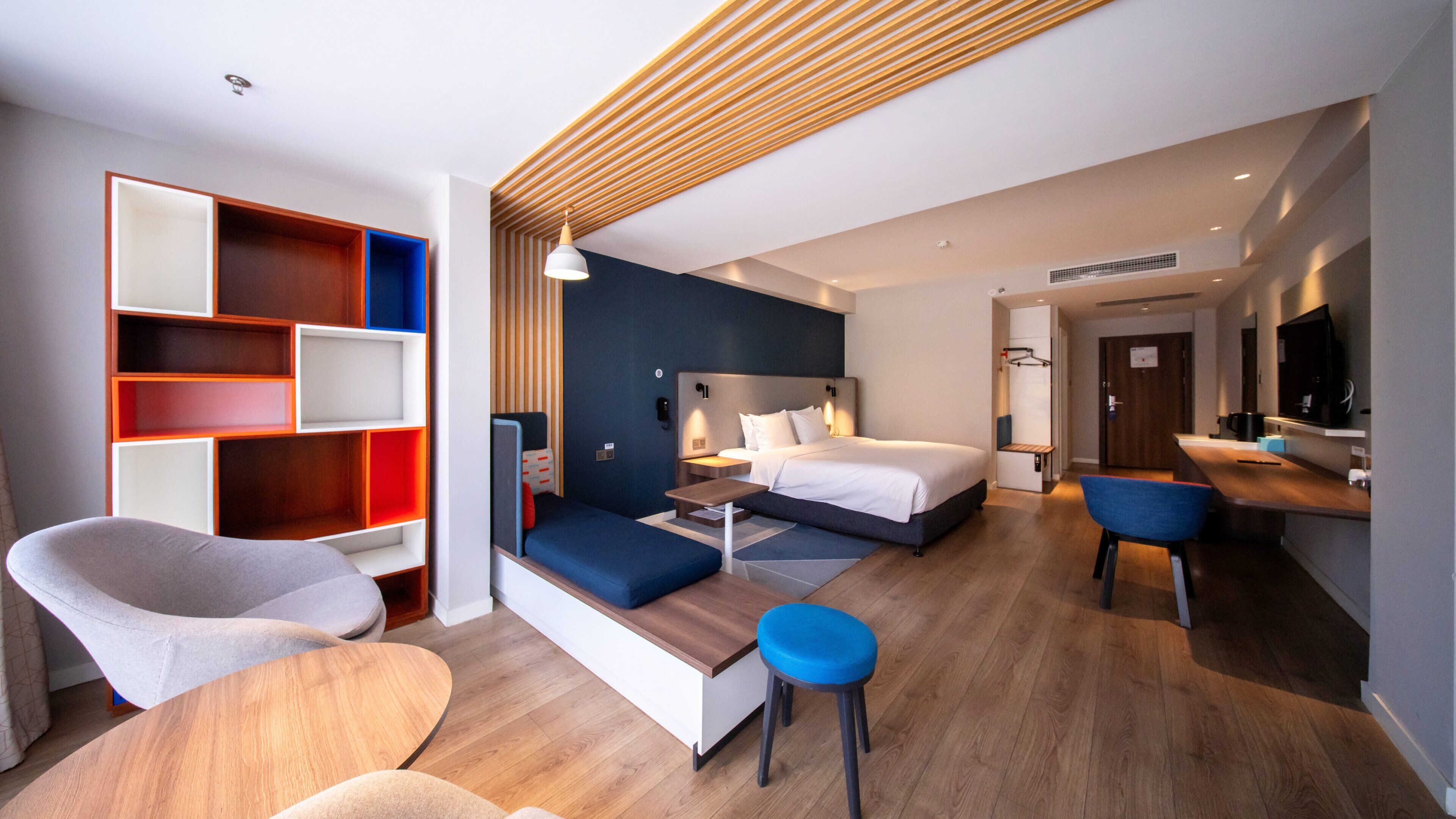 A modern hotel room with a bed, seating area, and a TV.