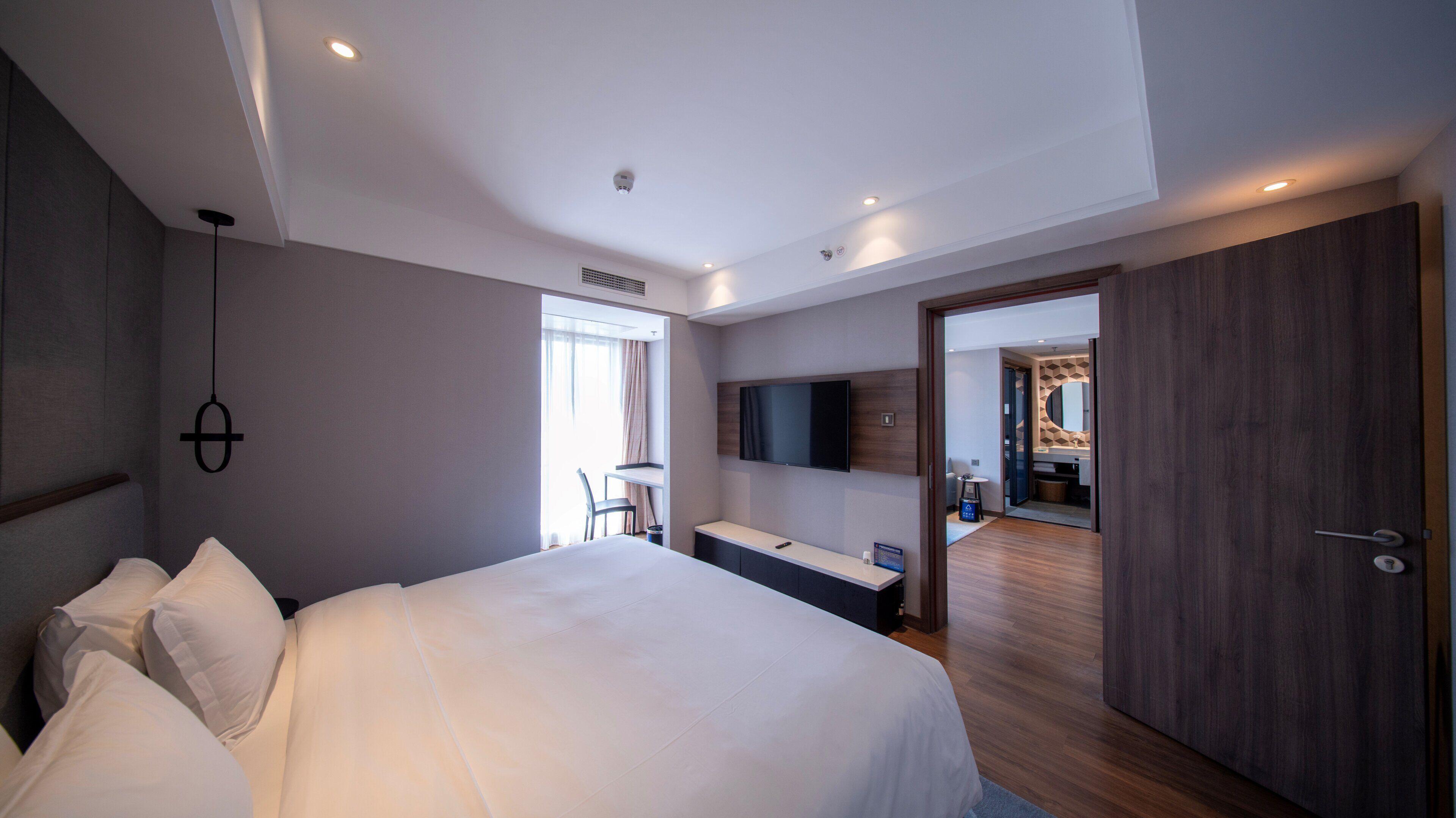 A modern hotel room with a large bed, a desk, a flat-screen TV, and a walk-in closet.