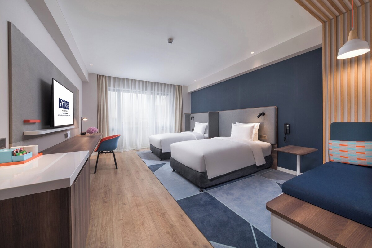 Una habitación de hotel moderna con dos camas, un escritorio y un televisor.