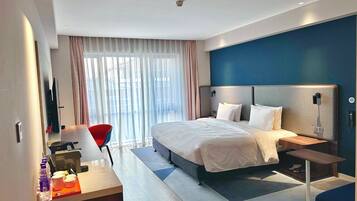 Una habitación de hotel moderna con una cama grande, mesitas de noche, un escritorio con silla, un televisor y una ventana con cortinas.