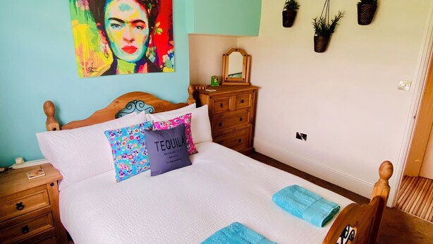 A bedroom with a wooden bed, two pillows, a mirror, a dresser, and hanging plants. - Characterful Home In Vibrant Village! (Scorton)