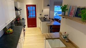 A compact kitchen with a red door, wooden flooring, and a small dining area with a table and chairs. - Characterful Home In Vibrant Village! (Scorton)
