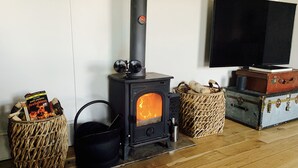 A wood-burning stove with a TV mounted on the wall, wicker baskets, and vintage suitcases. - Characterful Home In Vibrant Village! (Scorton)