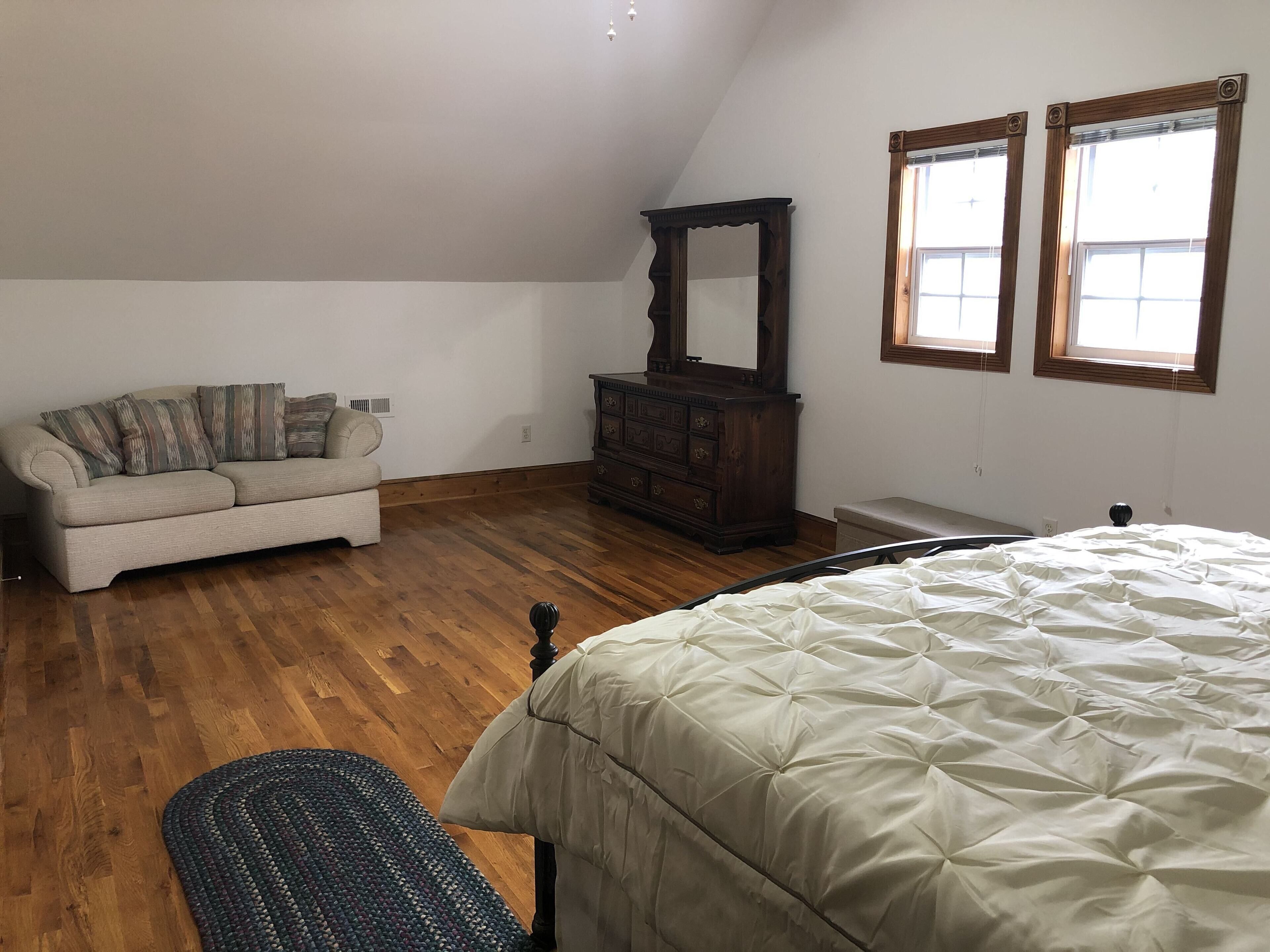 A bedroom with a bed, a sofa, a dresser, and two windows.