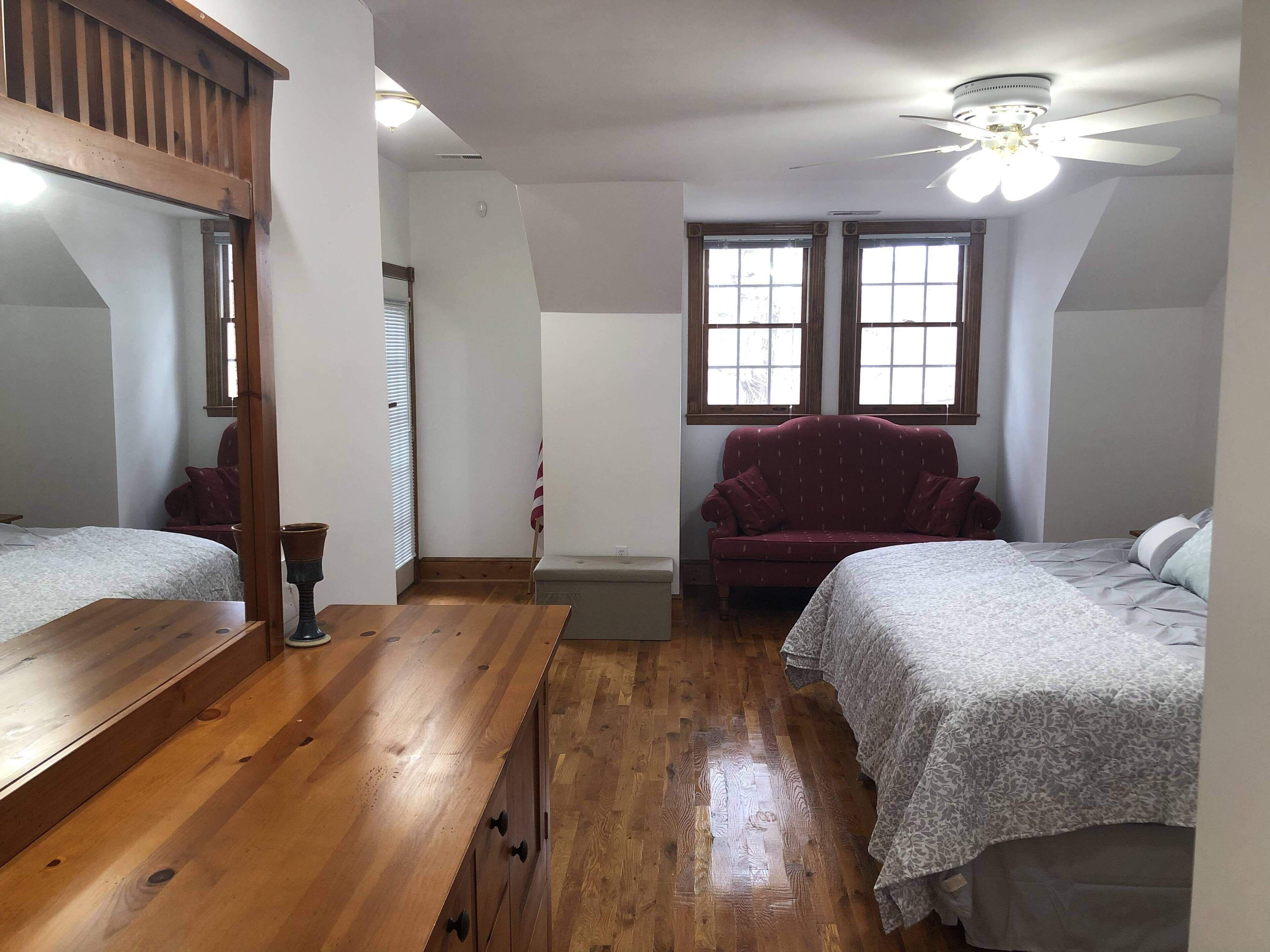 A bedroom with two beds, a wooden dresser, a red armchair, and a ceiling fan.