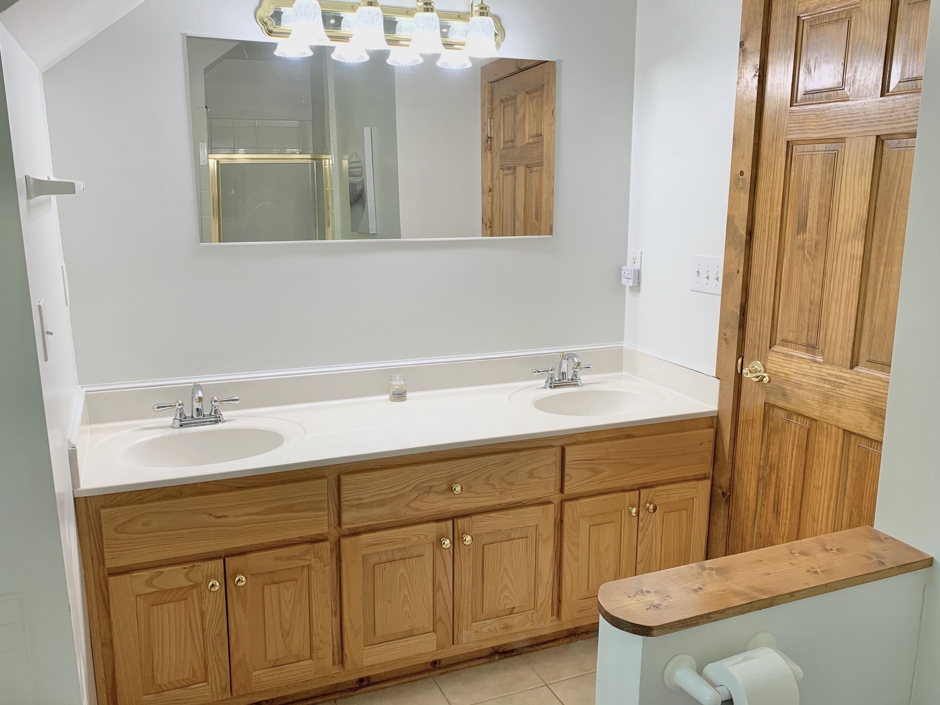 A bathroom with two sinks, wooden cabinets, a mirror, and a vanity with a towel rack.