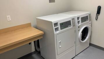 A laundry area with a washing machine and dryer, a wooden shelf, a phone, and a sign indicating cycle times.