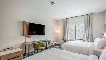 Ein Hotelzimmer mit zwei Betten, einem Schreibtisch, einem Stuhl, einem Fernseher und einem fenster mit Vorhängen.