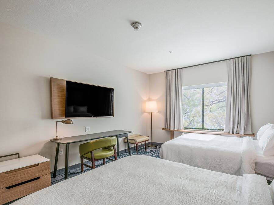 Quarto de hotel com duas camas, uma escrivaninha, uma cadeira, uma televisão e uma janela com cortinas.