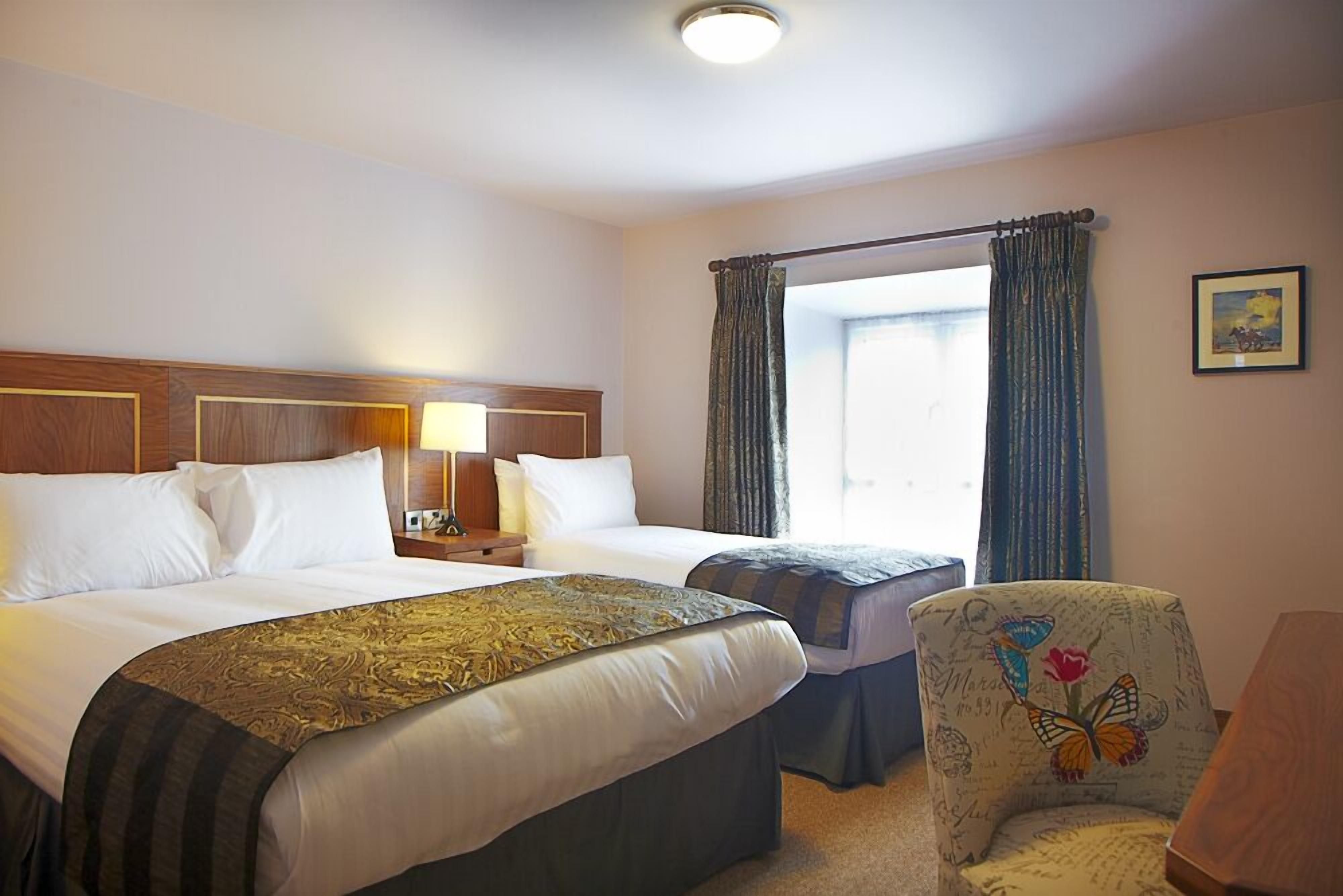 A hotel room with two beds, a nightstand, a chair with a butterfly design, and a window with curtains.