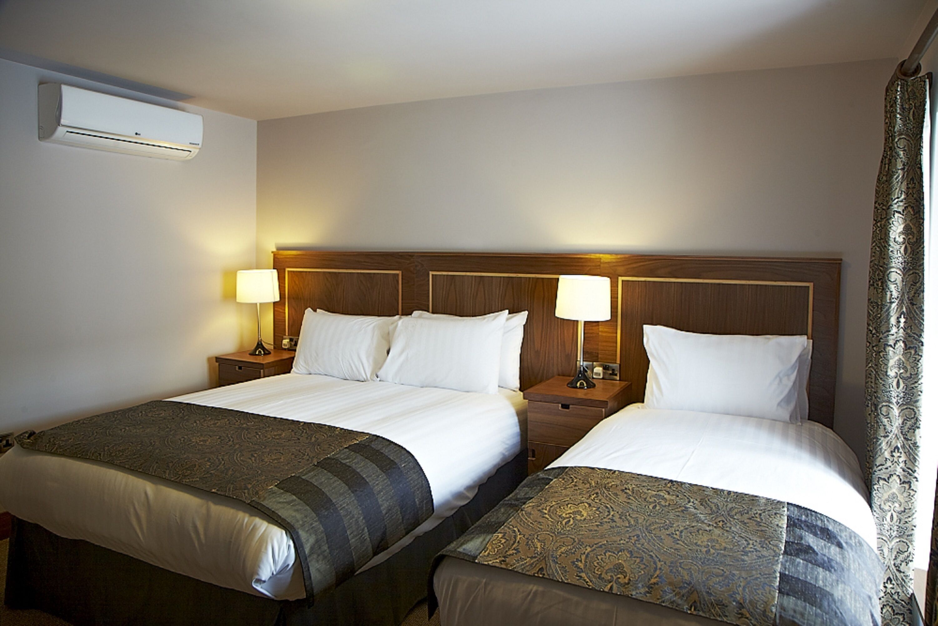 A hotel room with two beds, each with a wooden headboard, bedside lamps, and a blanket.