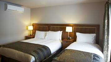 A hotel room with two beds, each with a wooden headboard, bedside lamps, and a blanket.