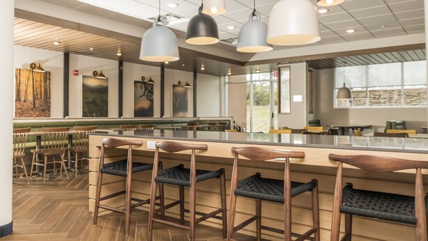 A modern bar area with wooden bar stools, pendant lighting, and artwork on the walls. - Fairfield Inn & Suites by Marriott Louisville New Albany IN (New Albany)