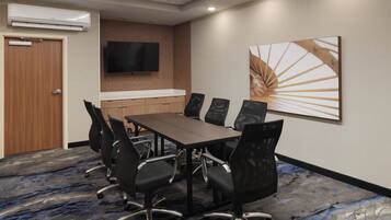 A conference room with a long table, six chairs, a flat-screen TV, and a large abstract painting on the wall.