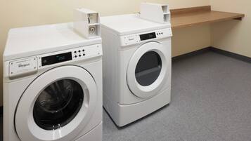 Deux machines à laver Whirlpool à chargement frontal se trouvent dans une buanderie, avec une étagère en bois au-dessus.