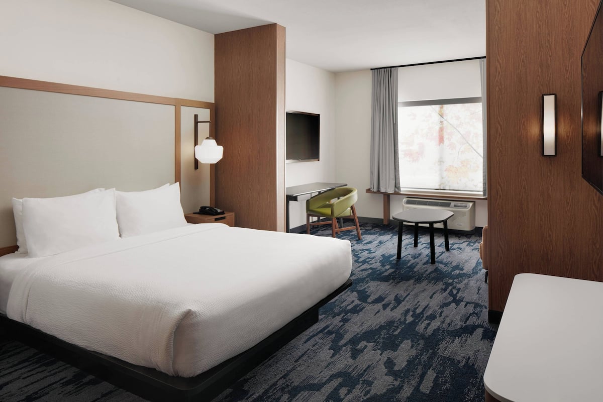 A hotel room with a large bed, a desk, a chair, a TV, and a window with curtains.
