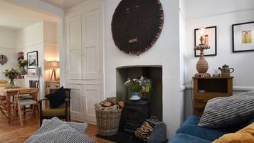 A cozy living room with a fireplace, a sofa, a dining table with chairs, and a bookshelf.