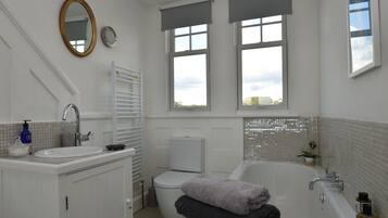 A bathroom with a sink, toilet, and bathtub. There are two windows with blinds, a mirror, and a towel rack.