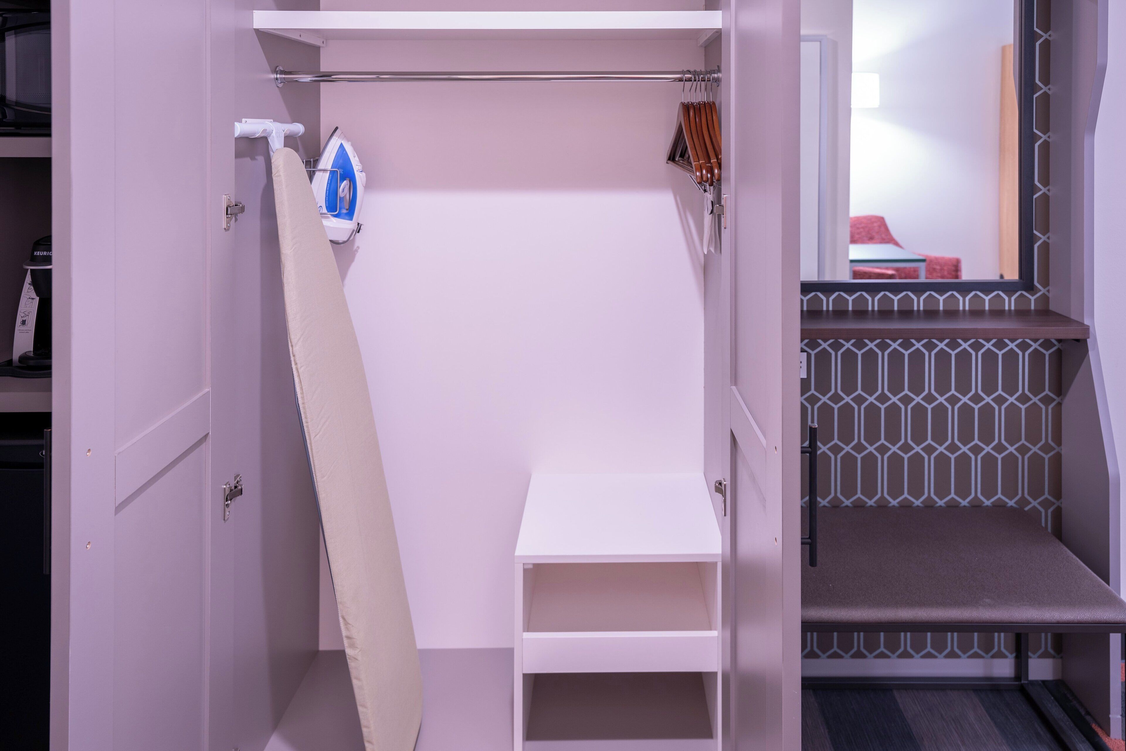 Ein Zimmer mit einem weißen Kleiderschrank, einem Bügeleisen und einer kleinen Ablagefläche.