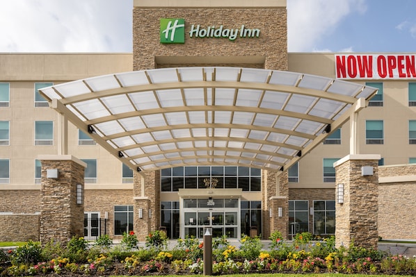 Eingang eines Holiday Inn Hotels mit überdachter Zugang, Steinfassade und einem Schild mit der Aufschrift 'ERÖFFNET'.