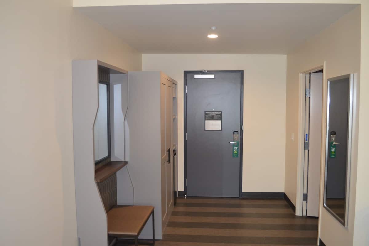 Un pasillo con una puerta, un banco y un estante fijado a la pared.