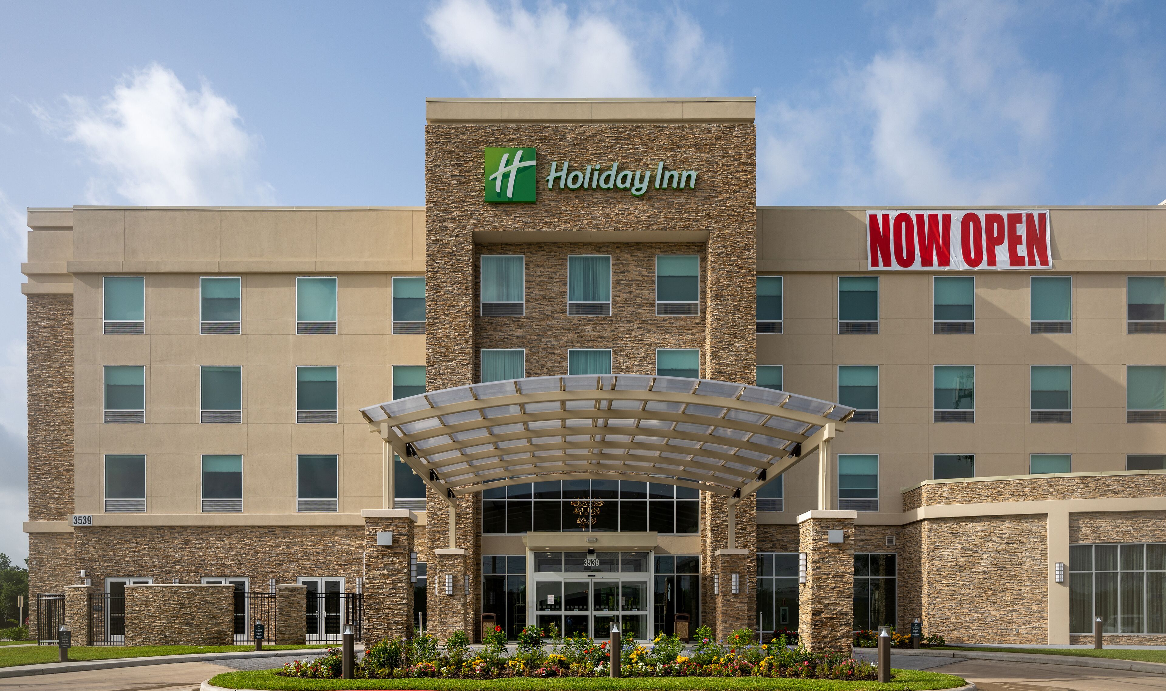 Un hôtel Holiday Inn avec une façade en pierre, une entrée couverte et une enseigne indiquant « OUVERT MAINTENANT ».