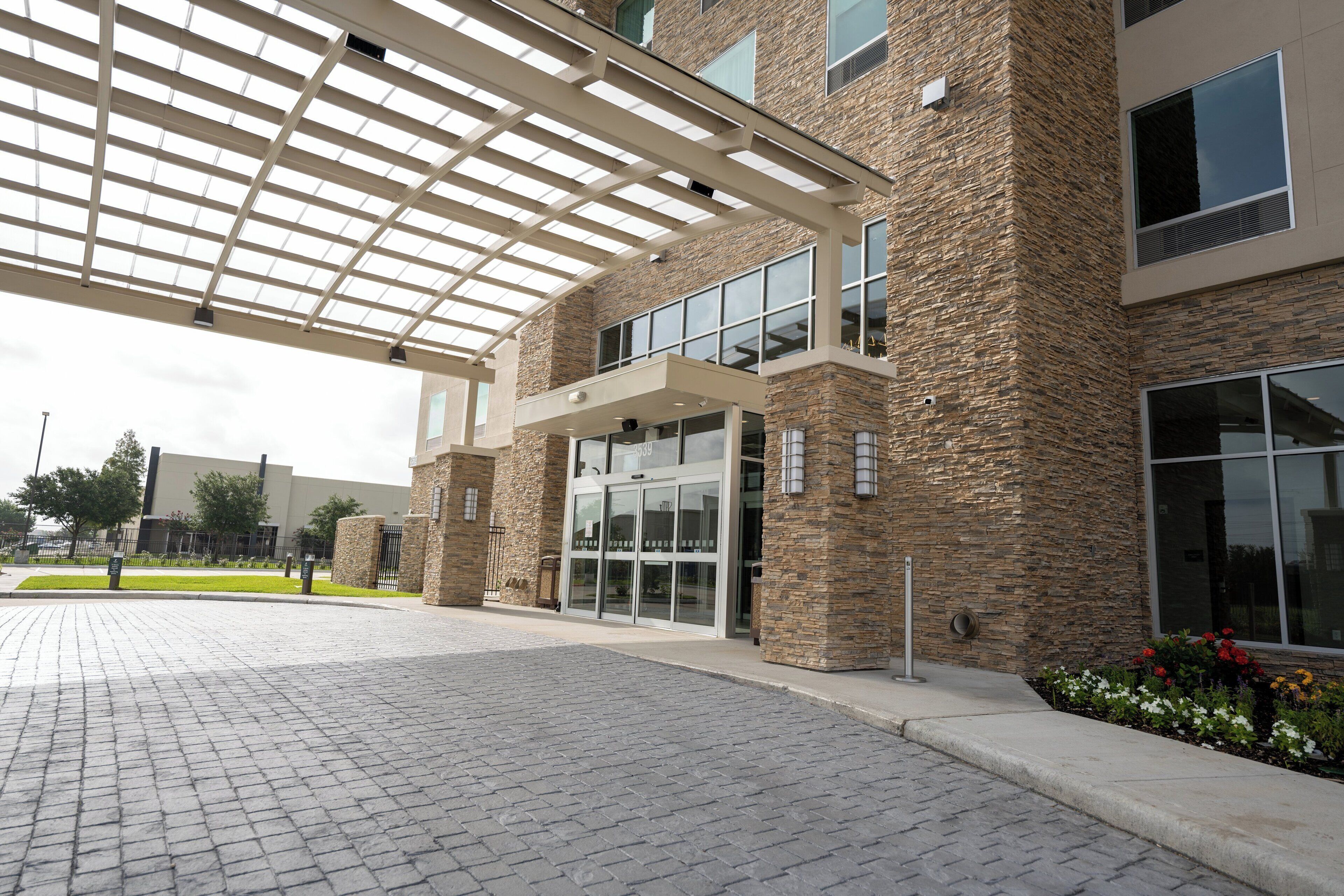 A building entrance with a covered walkway, stone facade, and glass doors.