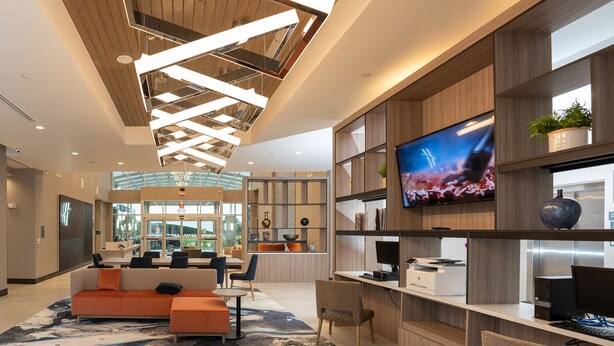 A modern hotel lobby with a reception desk, seating area, and a large TV screen. - Holiday Inn NW Houston Beltway 8 by IHG (Houston)