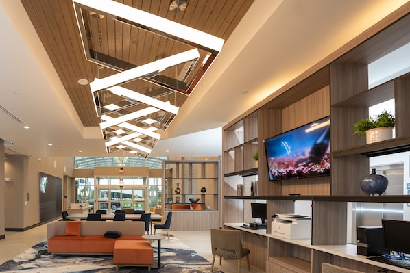 Een moderne hotel lobby met een receptiebalie, zithoek en een groot televisiescherm.
