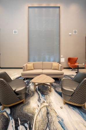 Een moderne zithoek met een beige bank, twee fauteuils, een klein rond tafeltje en een kamerkleed met een patroon.