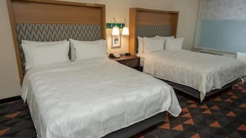 A hotel room with two beds, a nightstand with a phone and lamp, and a window with a view.
