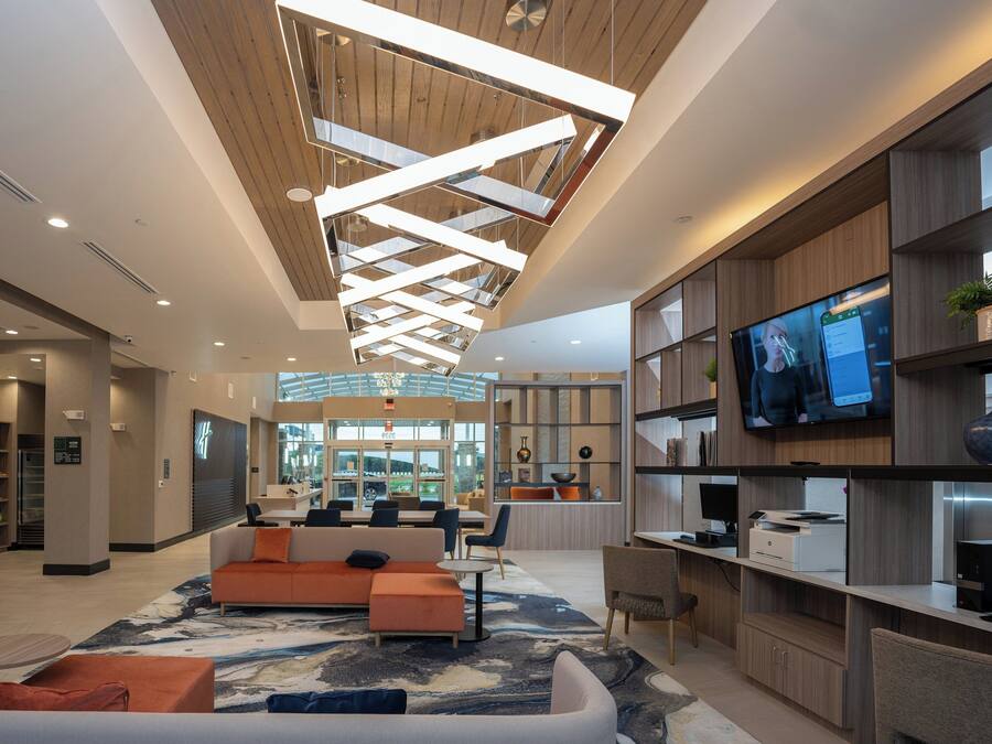 A modern lobby with a high ceiling, seating area, reception desk, and a large TV screen.