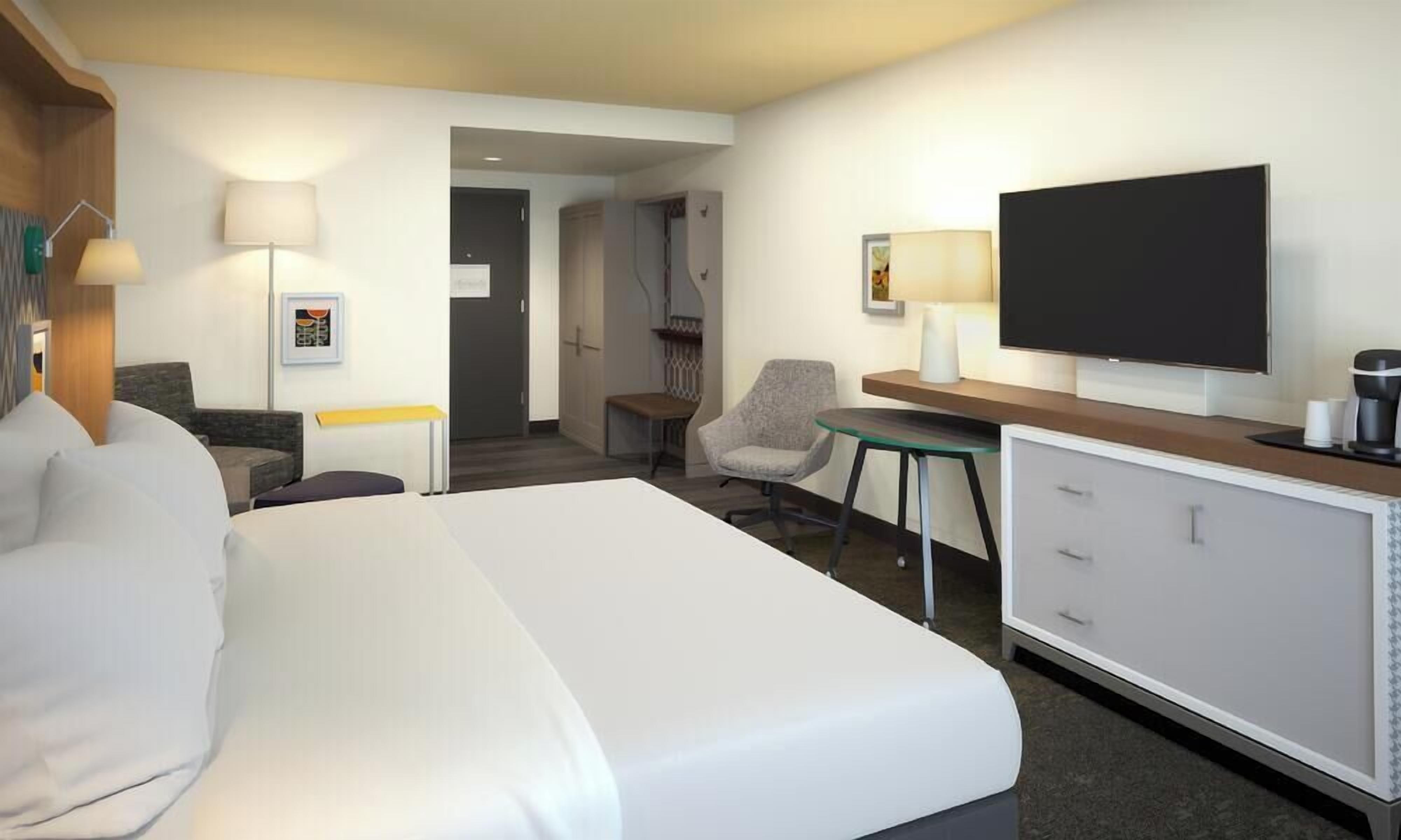 Una habitación de hotel con cama, escritorio, televisor y silla.