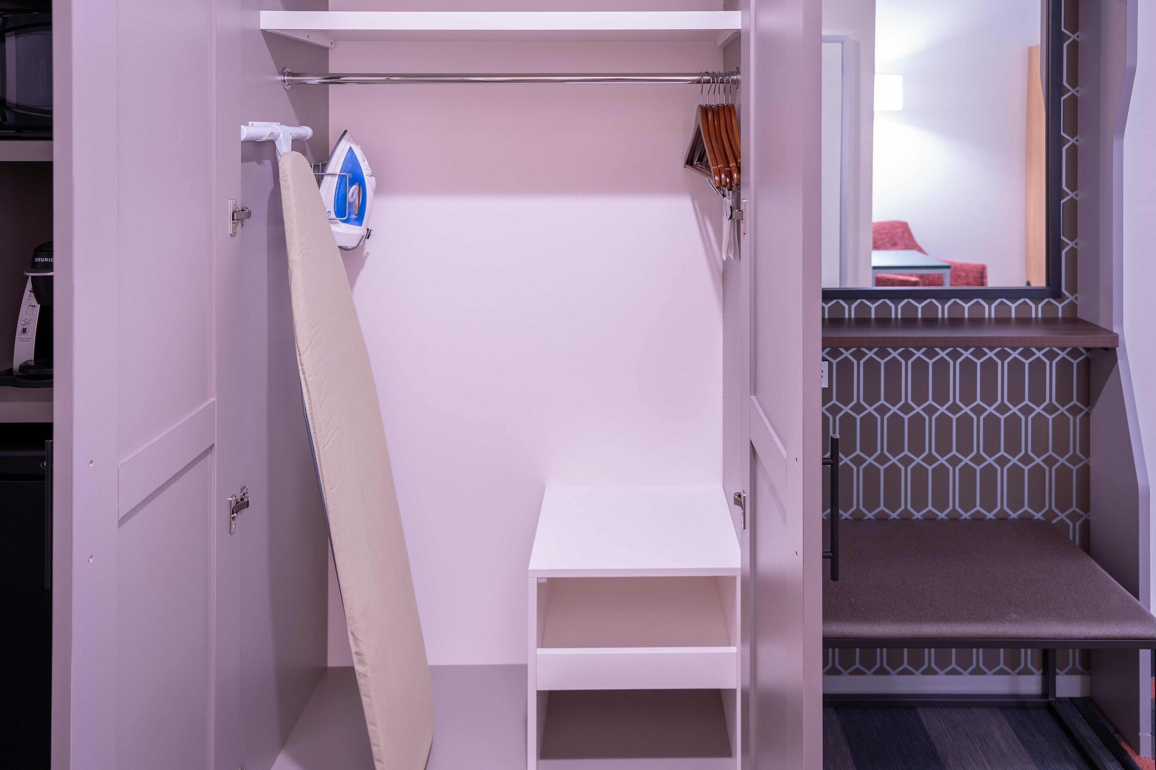 Una habitación compacta y moderna con una estación de planchado integrada, un pequeño rincón de descanso y una escalera con barandilla geométrica.