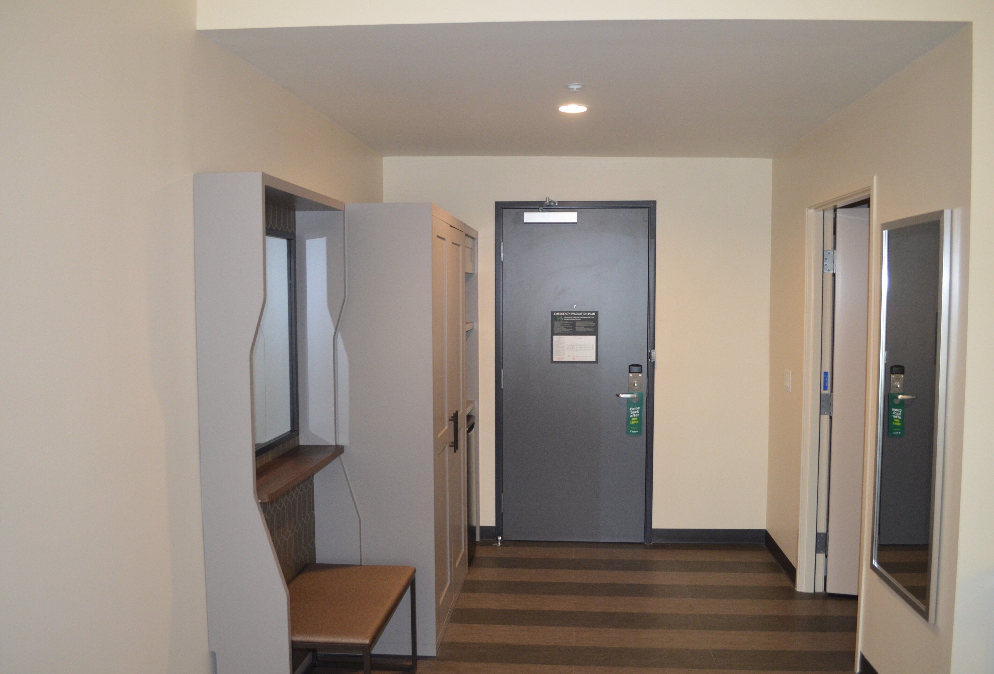 A hallway with a door, a bench, and a wall-mounted shelf.